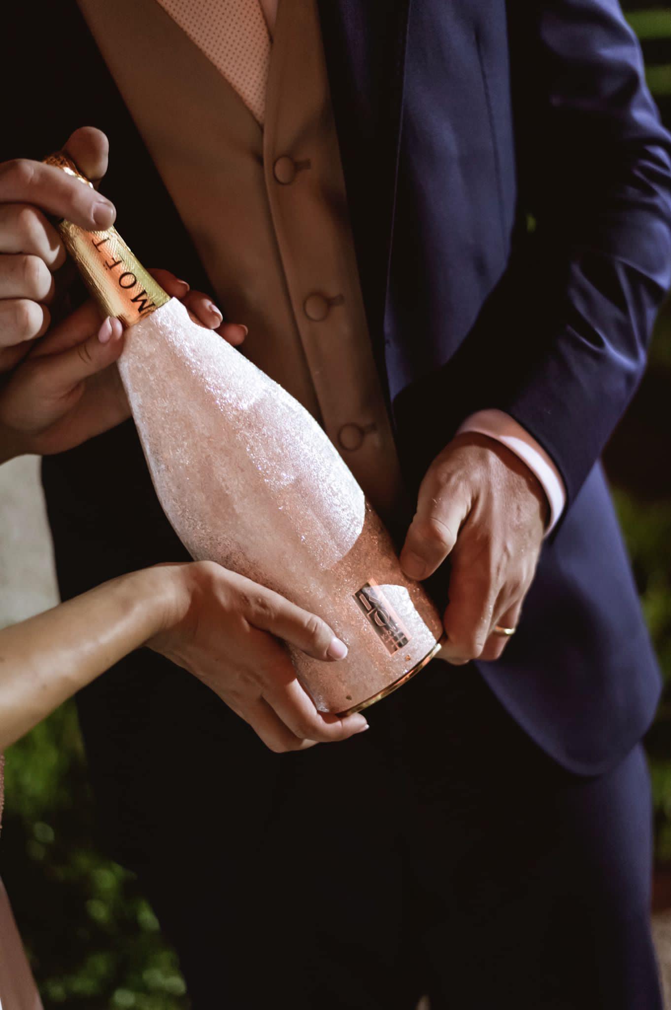Bride and groom holding a champagne bottle with an elegant textured silver cover during their wedding celebration.
