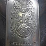 Close-up of hands engraving the Castello di Velona emblem onto a metallic champagne bottle cover.