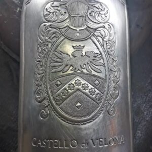 Close-up of hands engraving the Castello di Velona emblem onto a metallic champagne bottle cover.