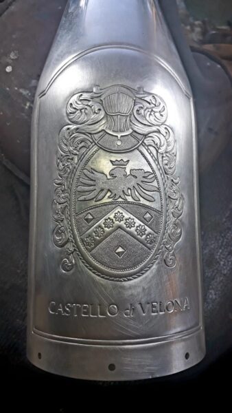 Close-up of hands engraving the Castello di Velona emblem onto a metallic champagne bottle cover.